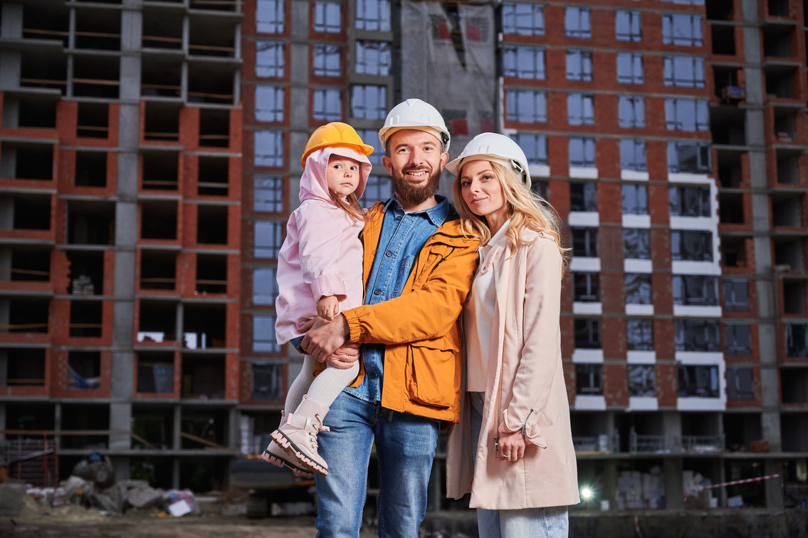 A tradie holding his young daughter, standing with his partner in front of a building site