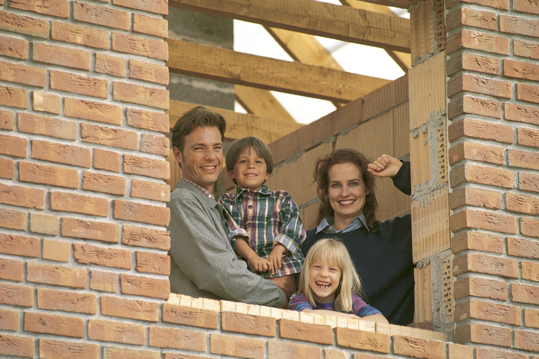 A builder and his family smiling through the timber frame of a new brick home